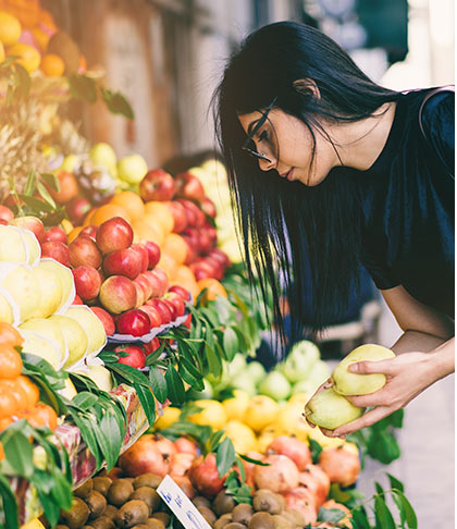 Stock image of woman with black hair, black tee shirt and glasses shopping in fruit section