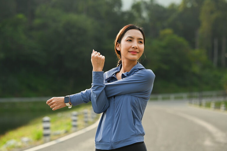 Sporty asian woman in sportswear stretching warming up her body before running in the green park
